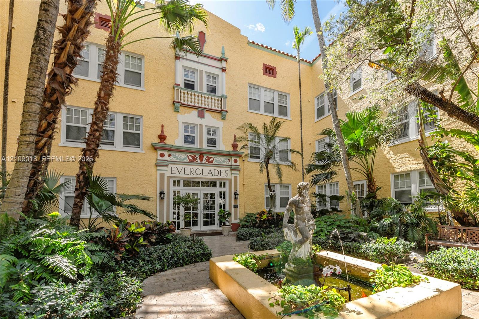 Mediterranean-style exterior featuring a stucco facade, decorative relief detailing, a central fountain with a sculptural centerpiece, and multi-pane windows