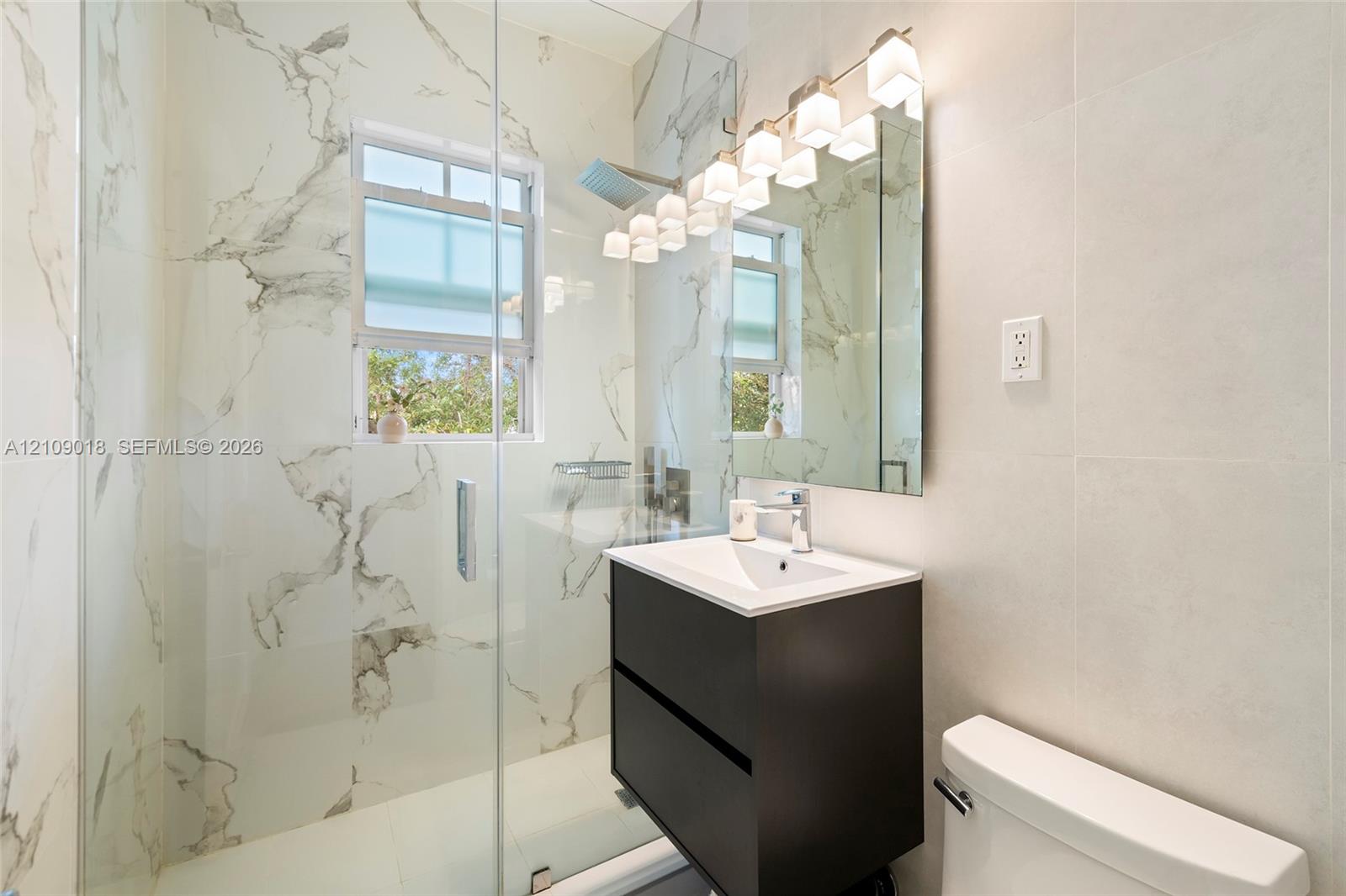 Walk-in shower with floor-to-ceiling large-format veined tile, wall-mounted vanity, multi-bulb vanity lighting, and rectangular undermount sink