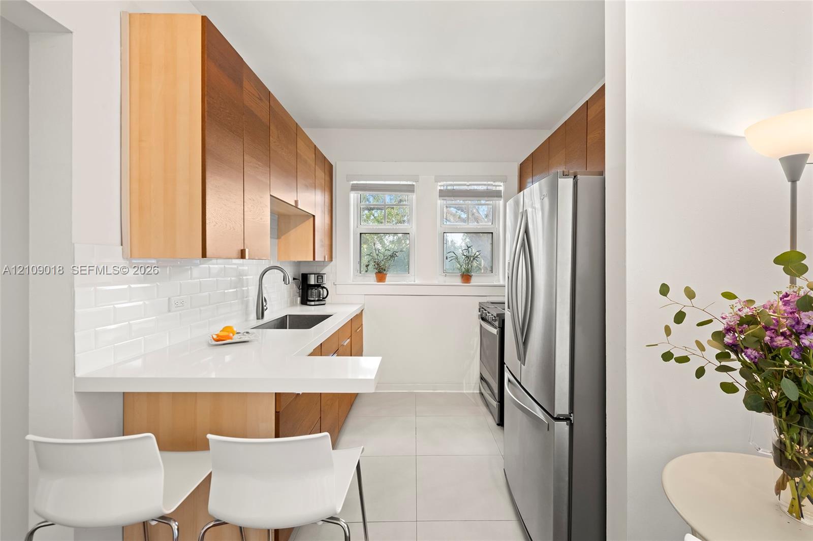 Kitchen featuring wood-finish cabinetry, white subway tile backsplash, solid-surface countertops with a breakfast bar, and stainless steel appliances
