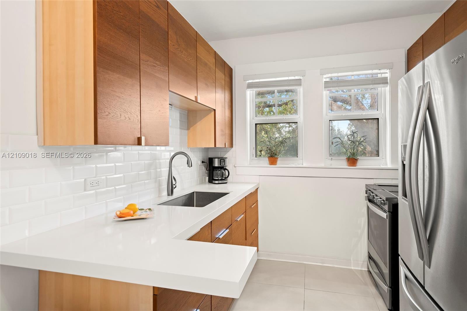 Kitchen featuring natural wood-finish cabinetry, white solid-surface countertops, white subway tile backsplash, stainless steel sink with gooseneck faucet, and stainless steel appliances