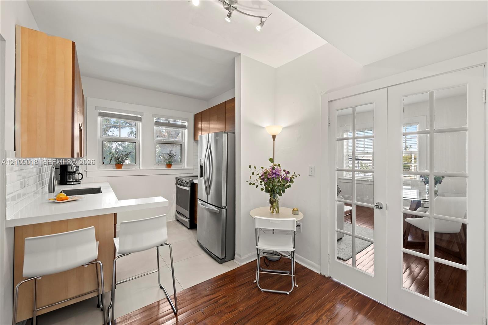 Kitchen featuring light wood-finish cabinetry, solid-surface countertops, subway tile backsplash, stainless steel appliances, and French doors with glass panes