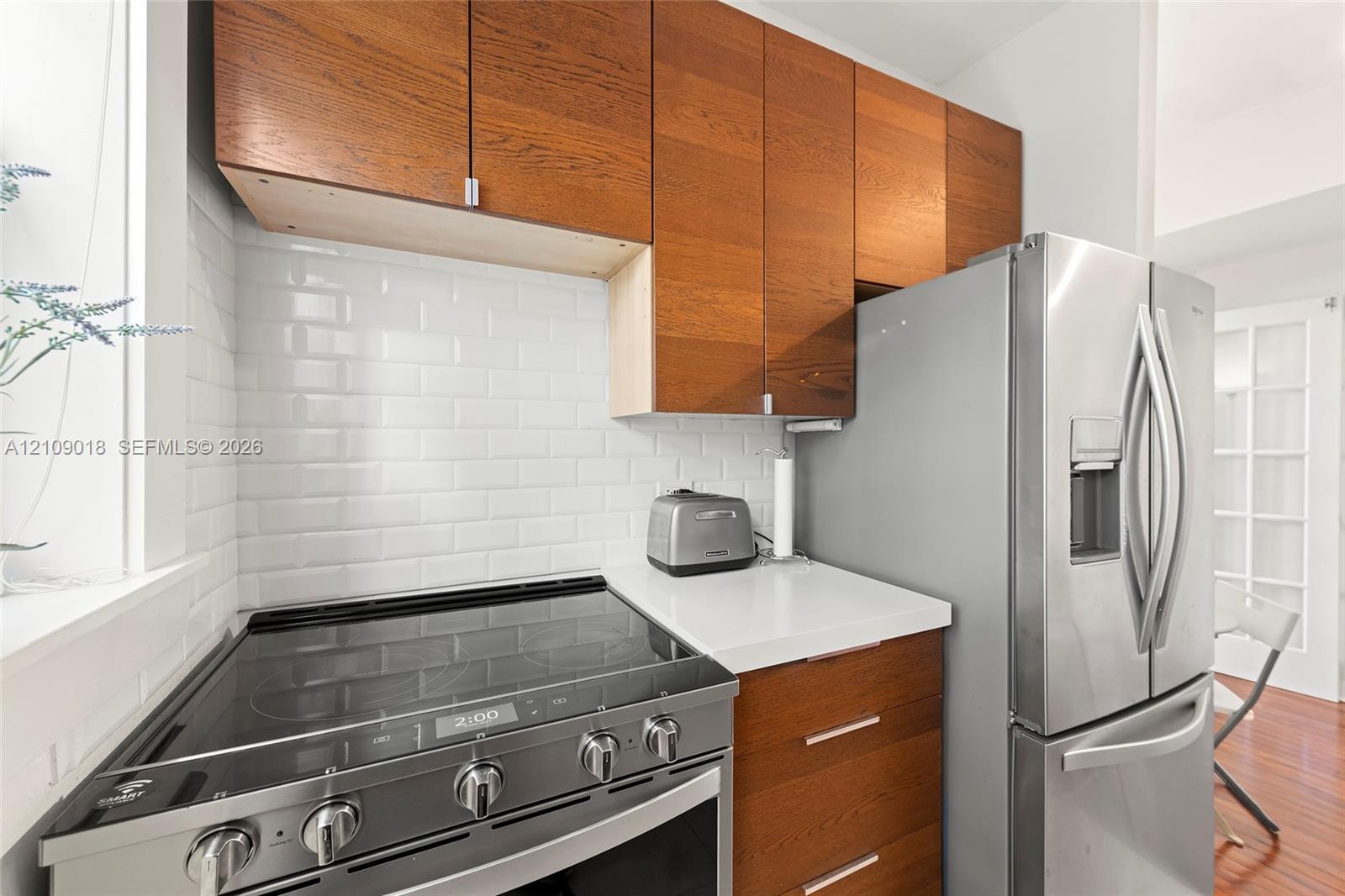 Kitchen featuring wood-finish cabinetry, white solid-surface countertops, a white subway tile backsplash, and stainless steel appliances