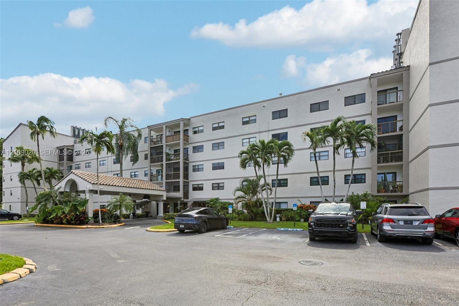 Multi-story stucco exterior featuring a covered porte-cochre with tile roofing, private recessed balconies, and mature palm landscaping