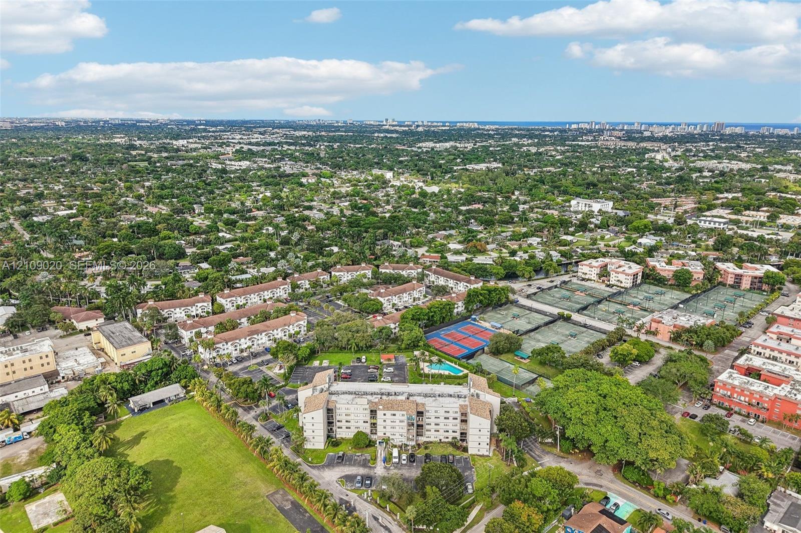 Aerial perspective of a multi-story residential building featuring an on-site swimming pool and hard-surfaced tennis courts