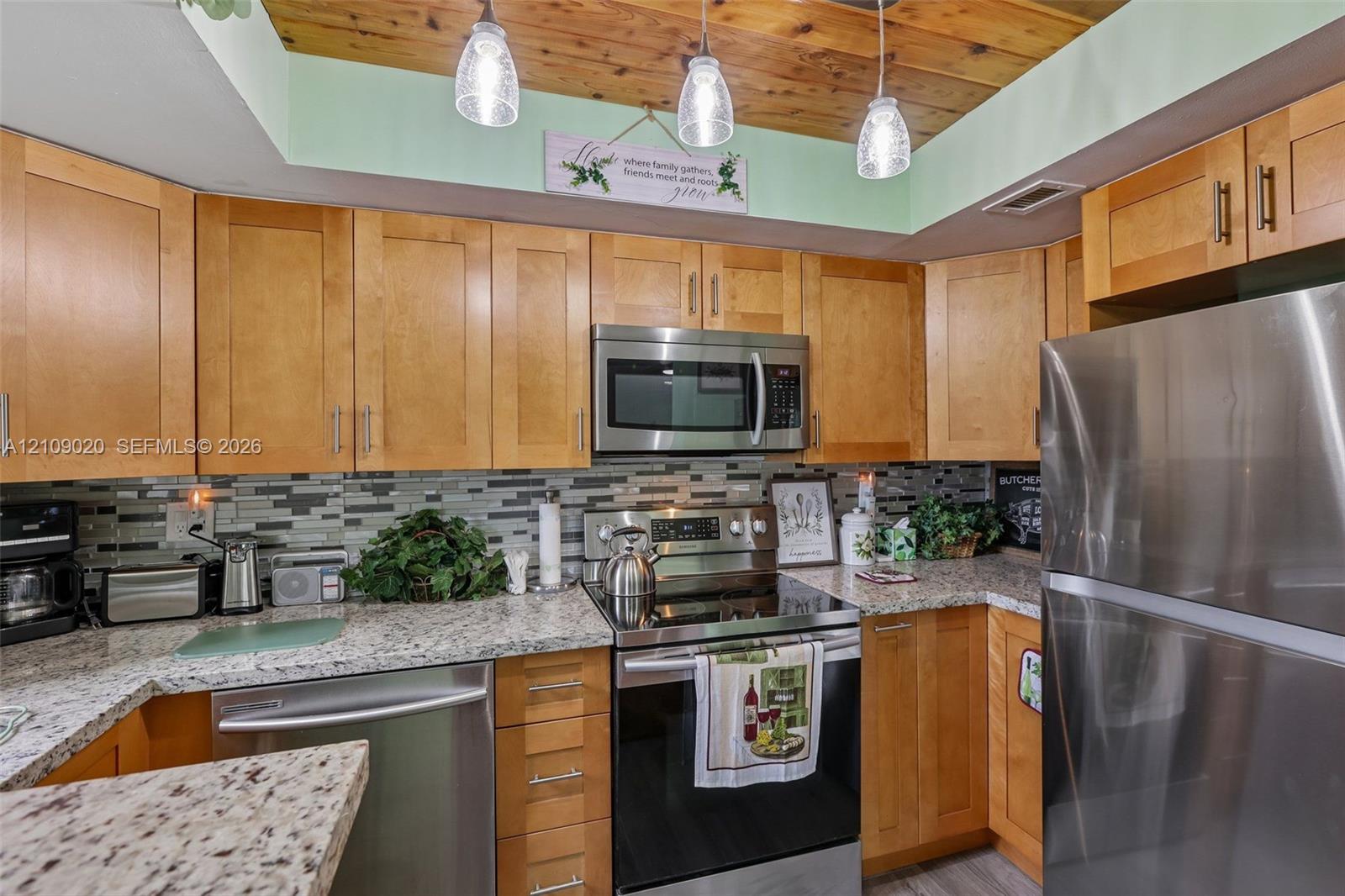 Kitchen featuring shaker-style wood cabinetry, stainless steel appliances, speckled stone countertops, a multi-tonal tile backsplash, and a wood-plank ceiling with pendant lighting