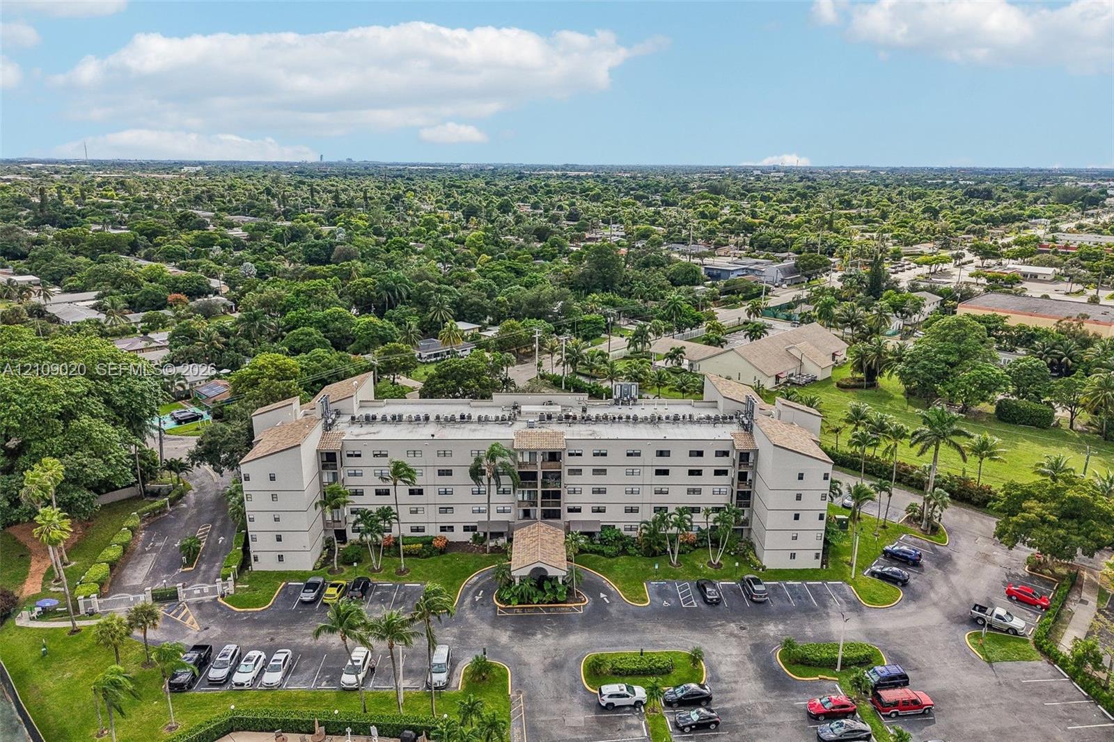 Multi-story residential building featuring a covered entryway, paved surface parking, and manicured landscaping with mature palm trees