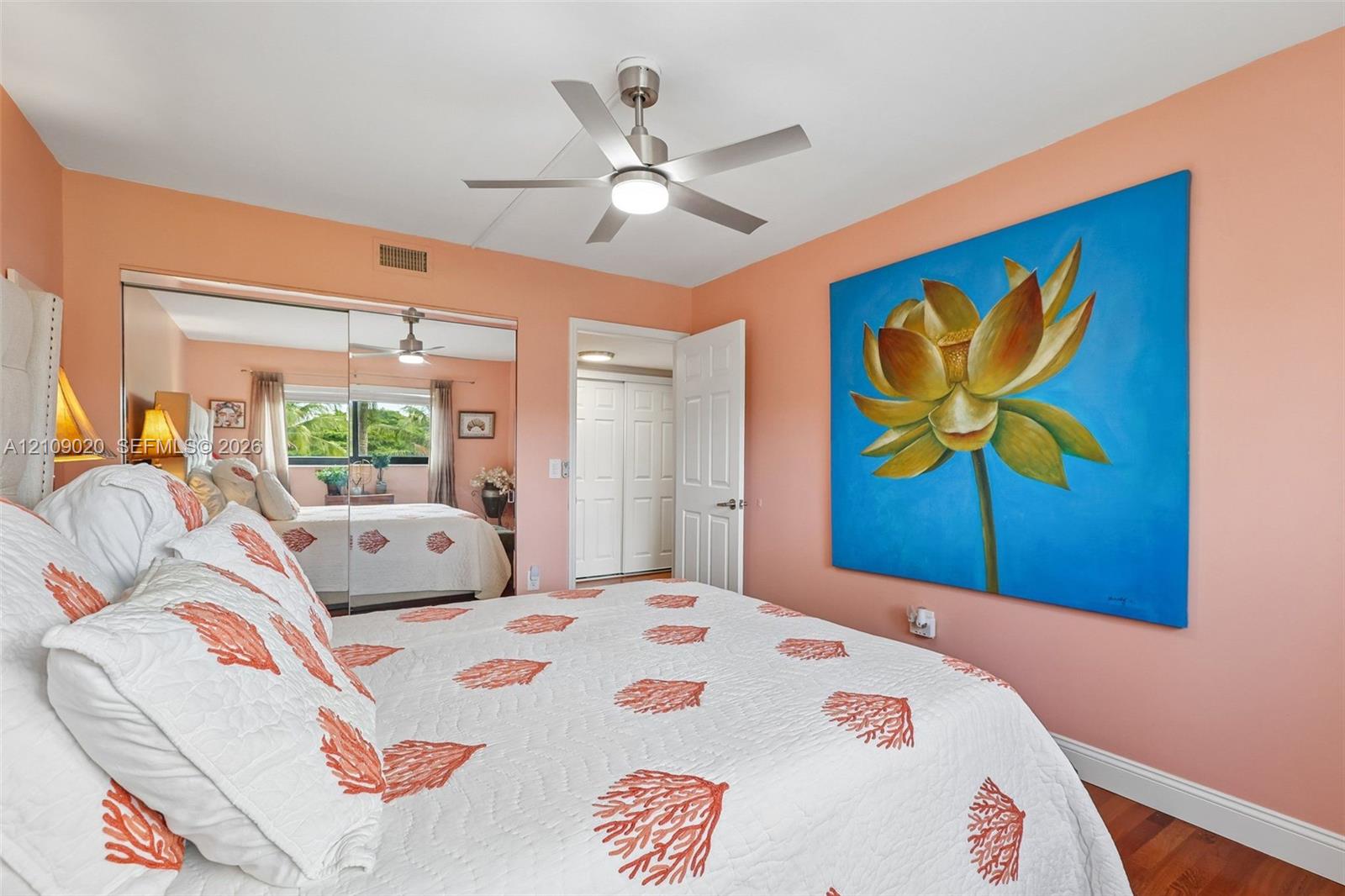 Bedroom featuring wood-finish flooring, a brushed nickel ceiling fan with integrated lighting, and mirrored closet doors