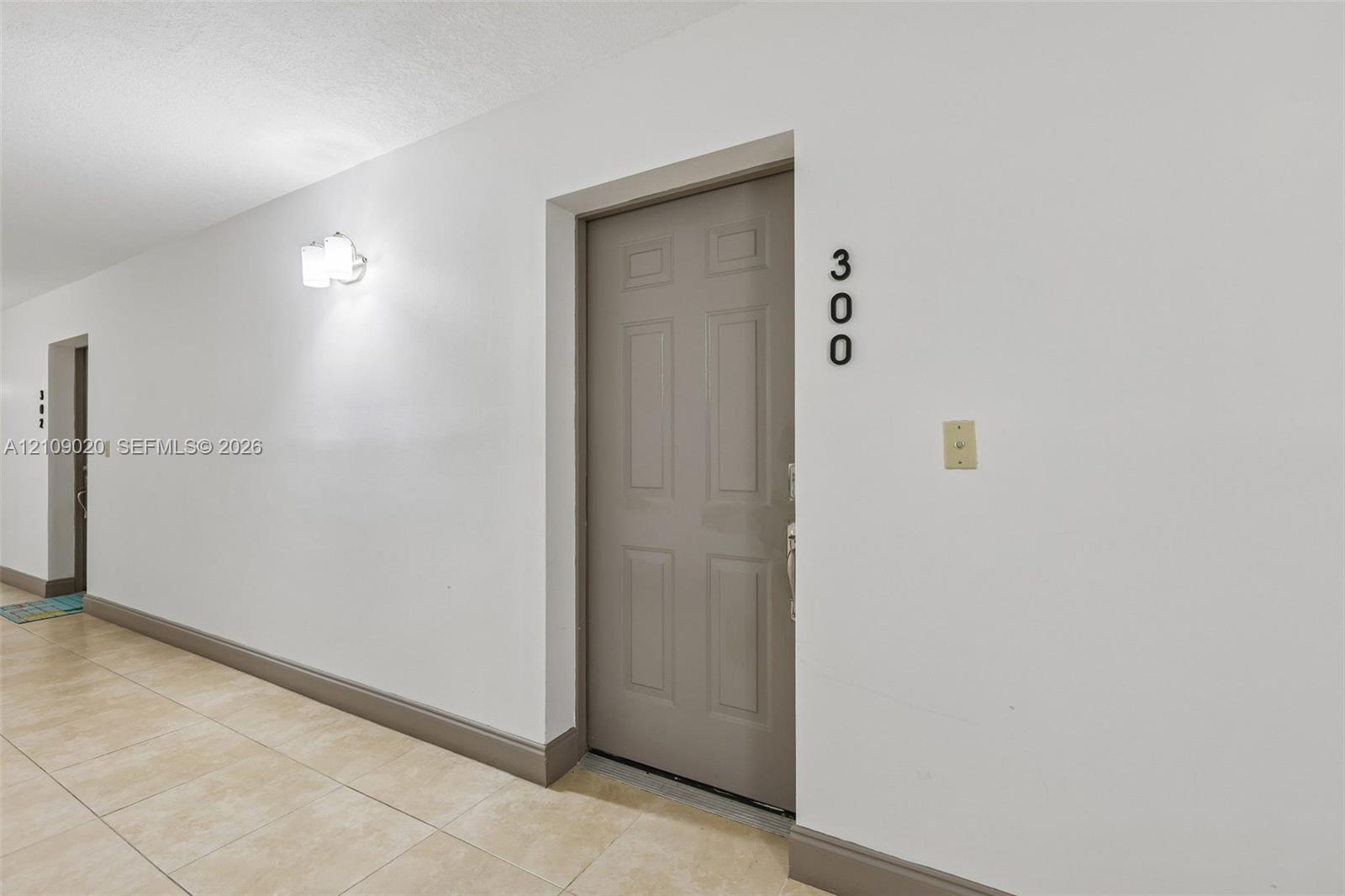 Six-panel entry door with polished hardware, neutral tile flooring, and wall-mounted light fixture
