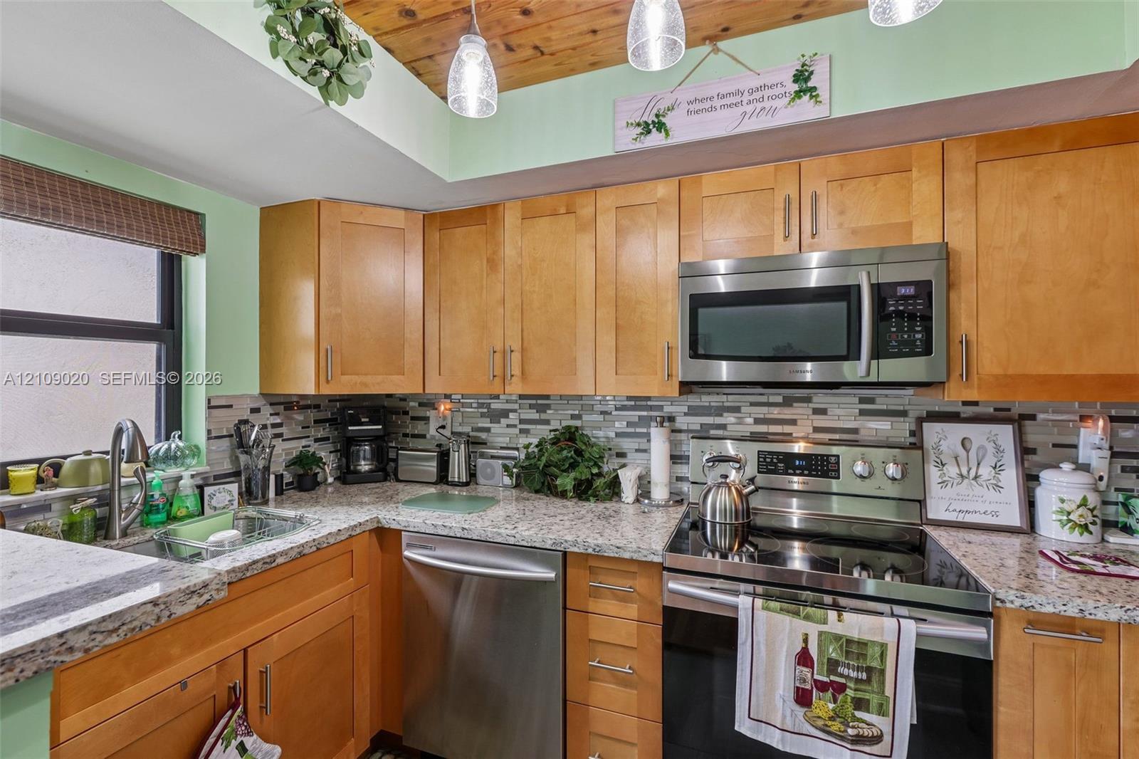 Kitchen featuring natural wood cabinetry, stone-finish countertops, stainless steel appliances, multi-toned tile backsplash, and wood-paneled ceiling with pendant lighting