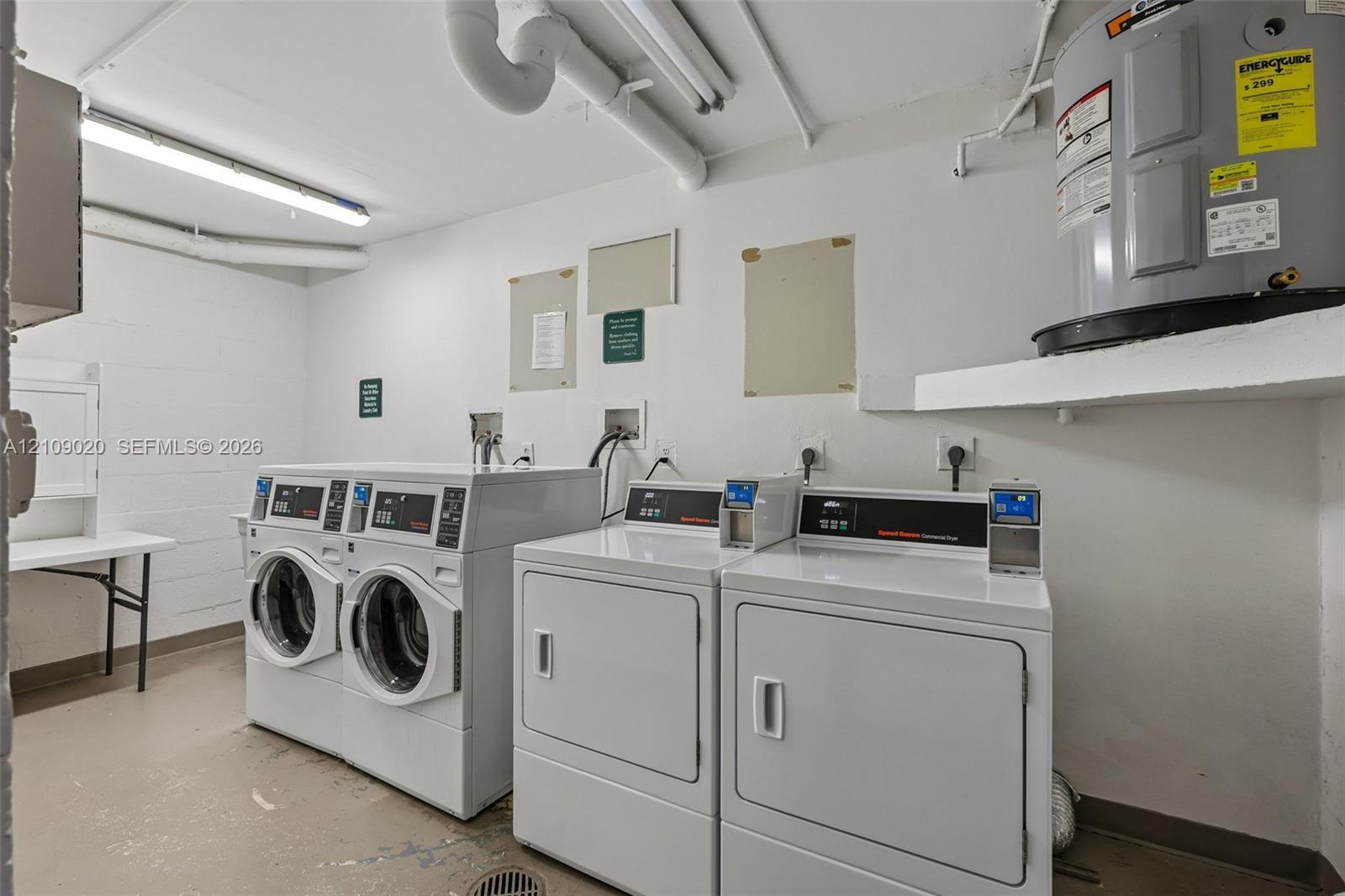 Utility space featuring two front-loading washers, two commercial-grade dryers, wall-mounted water heater, and fluorescent lighting