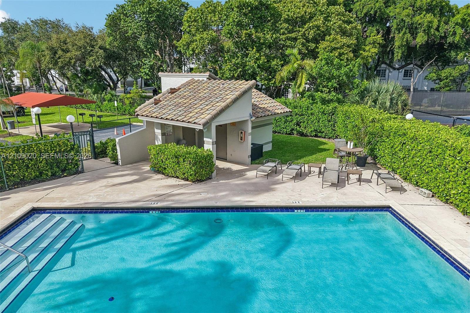 Swimming pool with tile edging and built-in stairs, concrete pool deck, tile-roofed cabana, and manicured perimeter hedges