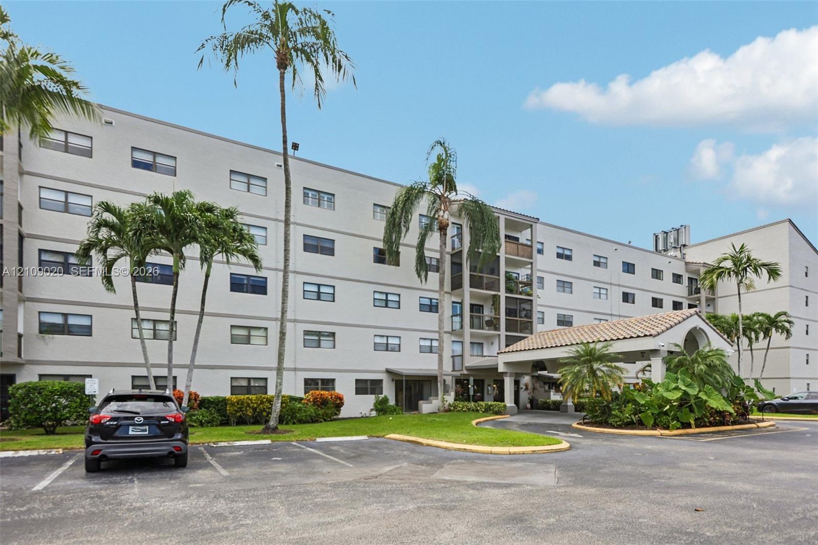 Multi-story residential building exterior featuring a covered porte-cochre, tiled roof detailing, and established palm trees