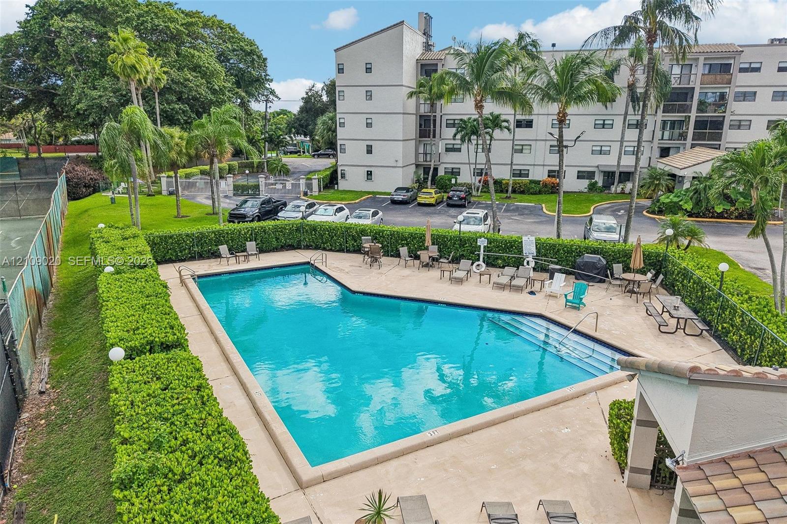 In-ground swimming pool featuring a concrete deck and perimeter hedge landscaping, inclusive of a tennis court facility
