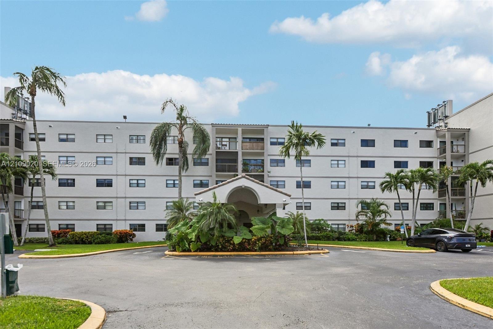 Multi-story stucco exterior featuring a covered entryway, private balconies, and landscaped grounds with mature palm trees