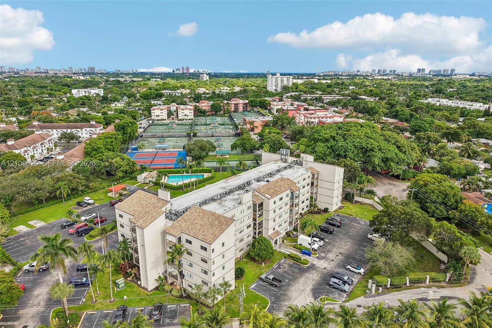 Multi-story residential building featuring shingled rooflines, exterior parking areas, and mature landscaping