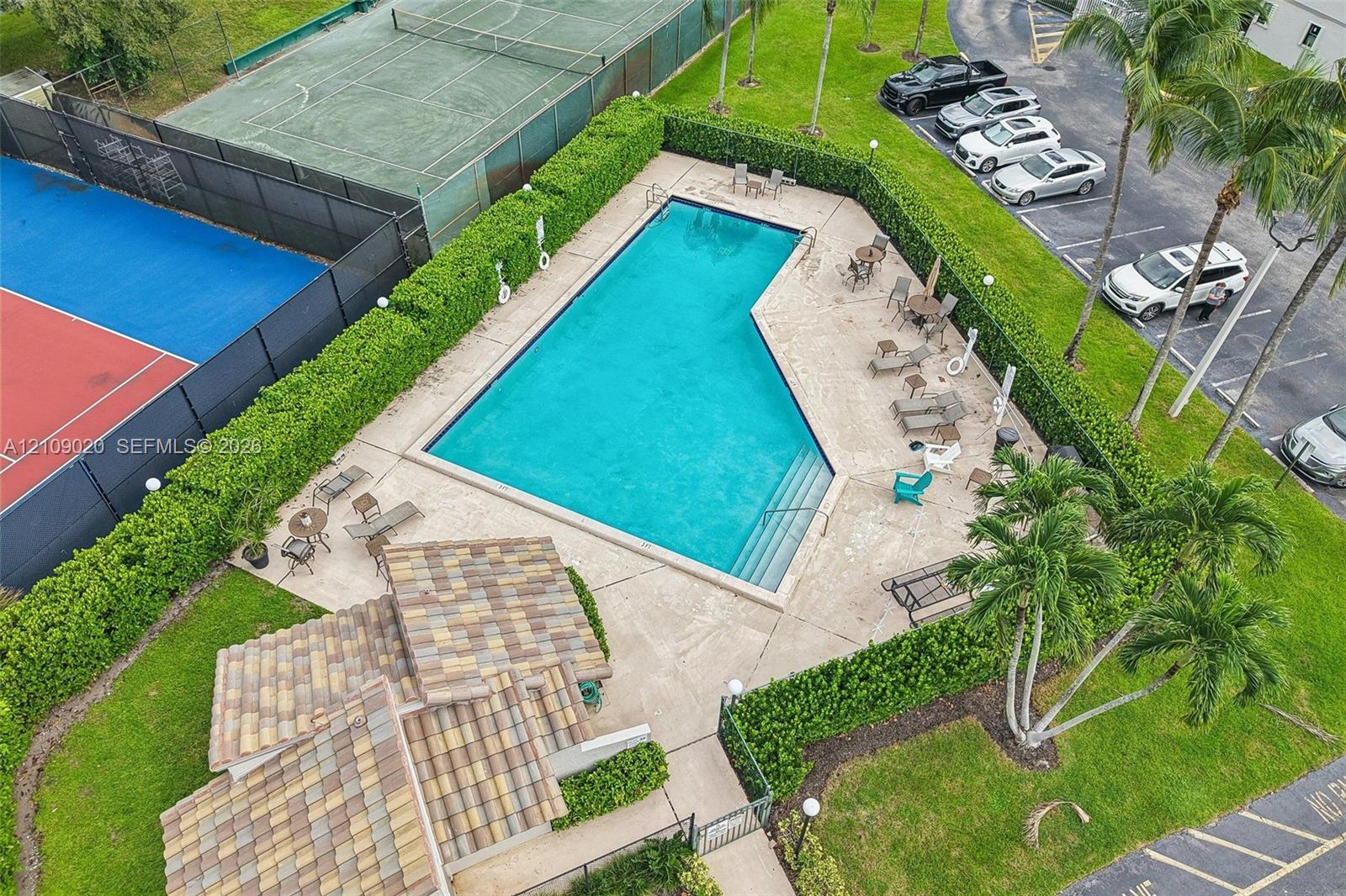 Swimming pool with integrated stairs, tennis court, tiled pavilion structure, paved deck, and perimeter landscaping