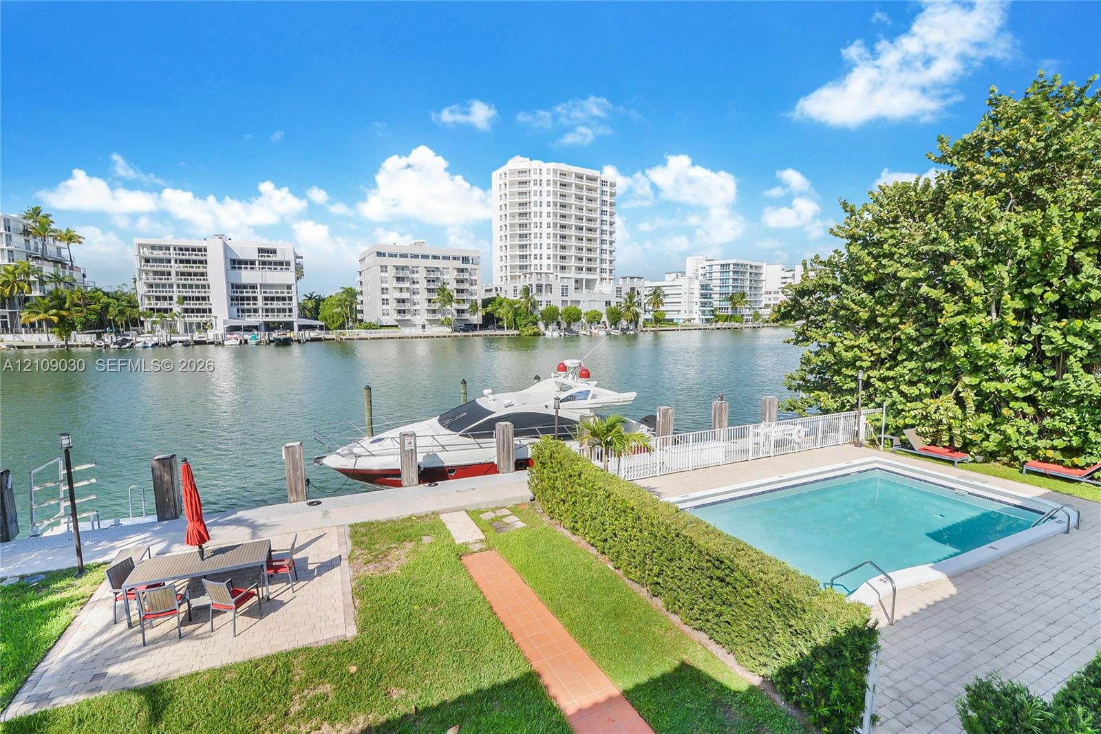 Waterfront property featuring a private boat dock, in-ground swimming pool, manicured lawn, and stone paver patio