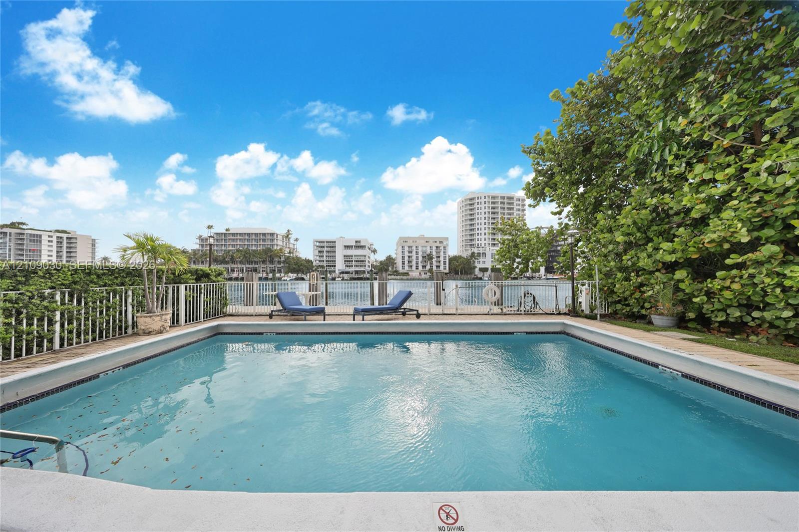 In-ground swimming pool featuring a light-colored perimeter coping, vertical metal safety fencing, and a bulkhead dock along the waterfront