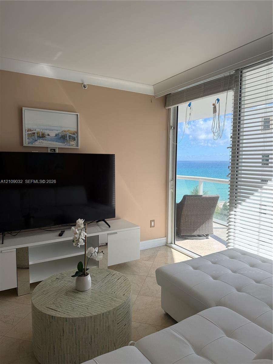 Floor-to-ceiling sliding glass doors with horizontal blinds, stone flooring, and balcony access with ocean horizon scenery