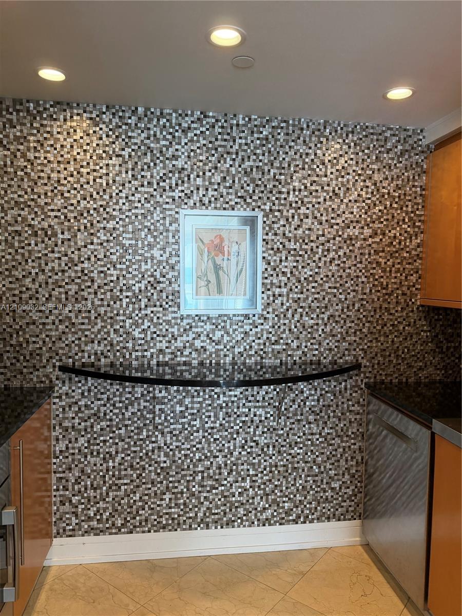 Mosaic tile accent wall featuring a curved stone-finish ledge, flat-panel cabinetry, stainless steel appliances, and recessed lighting