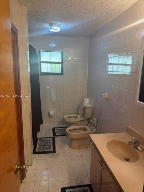Bathroom featuring floor-to-ceiling tiled walls, tiled flooring, a built-in vanity with an integrated basin, and a private bidet