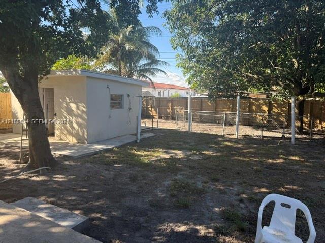 Backyard featuring a standalone stucco structure, concrete patio, perimeter wood fencing, and mature trees