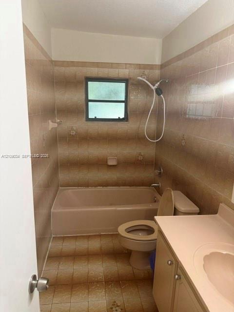 Full bathroom featuring a tub-shower combination with a handheld showerhead, textured tile wall surround, integrated vanity countertop with a recessed basin, and tile flooring