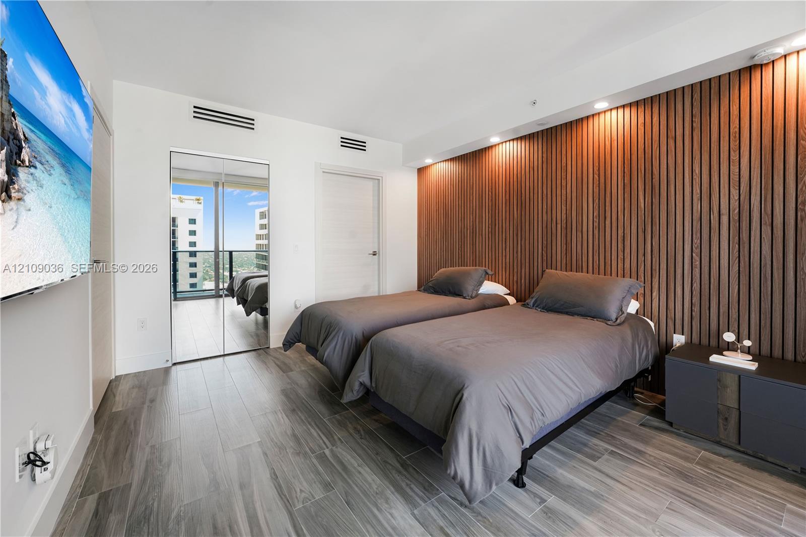 Interior room featuring a wood-slat accent wall, wood-finish flooring, recessed ceiling lighting, and a floor-to-ceiling glass door providing exterior balcony access