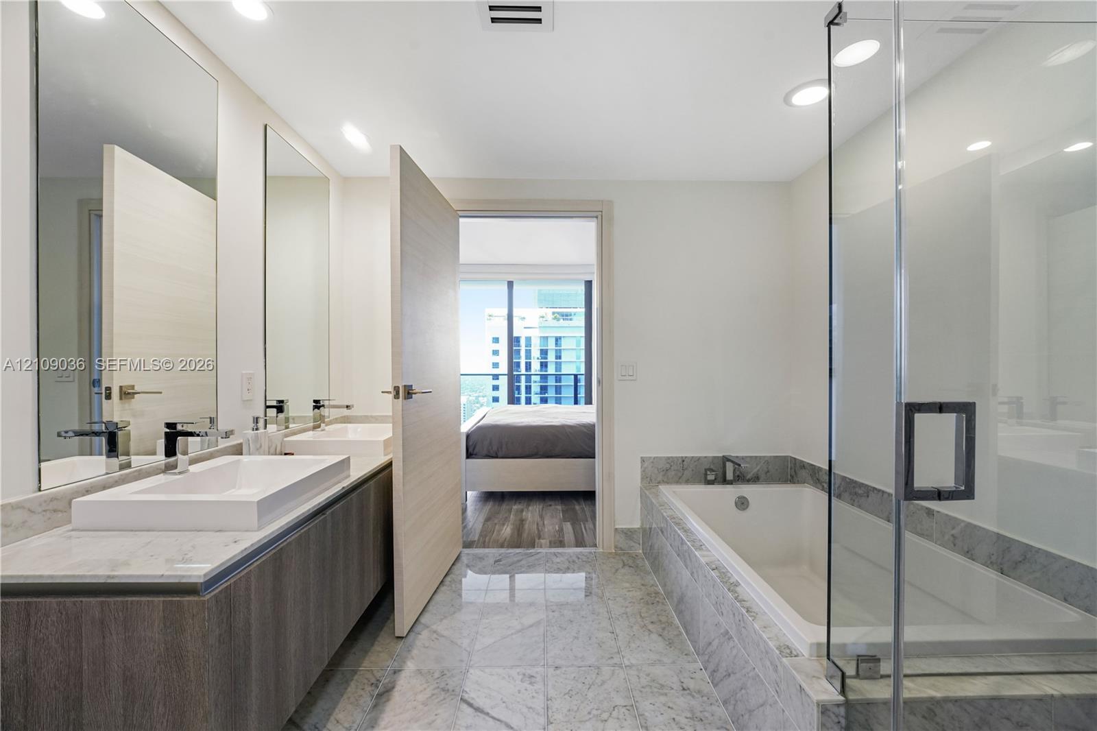 Double vanity featuring rectangular vessel sinks and stone-surround countertop, stone tile flooring, deep soaking tub, and a glass-enclosed shower