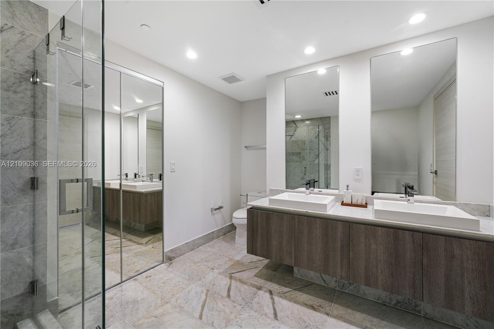 Floating double vanity with rectangular vessel sinks, floor-to-ceiling tiled glass-enclosed shower, stone-finish flooring, and dual wall-mounted mirrors