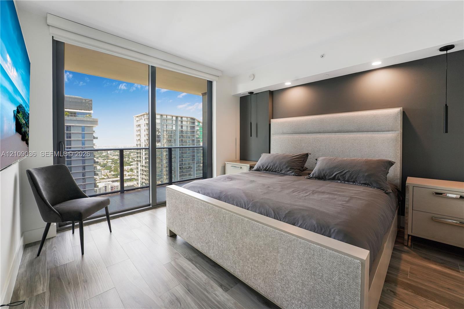 Floor-to-ceiling glass sliding doors, private balcony with metal railing, wood-finish flooring, and recessed ceiling lighting