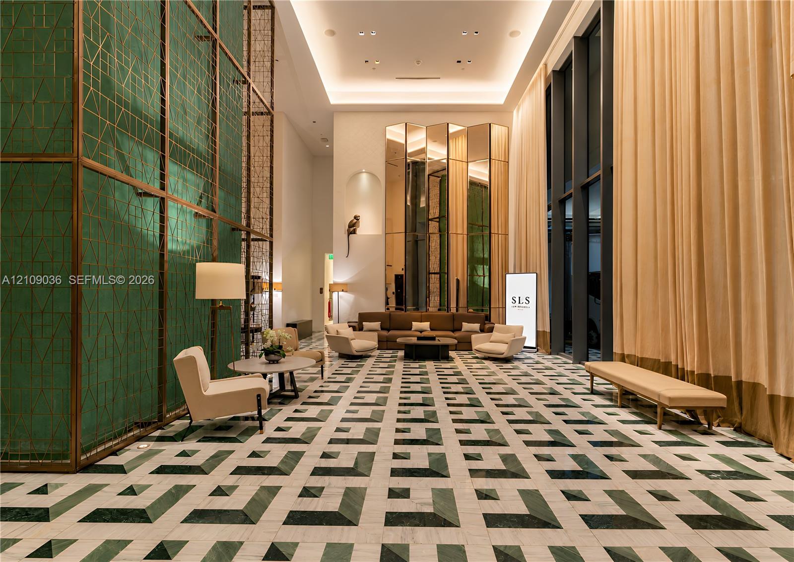 Grand lobby featuring double-height ceilings, intricate green geometric wall cladding, full-height window treatments, and patterned stone flooring