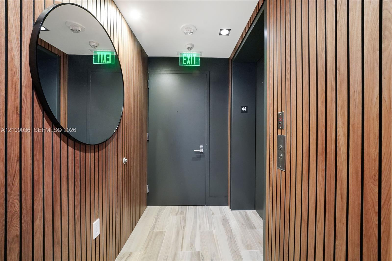 Vertical wood-slat wall paneling, light wood-finish flooring, recessed ceiling lighting, and a circular wall-mounted mirror