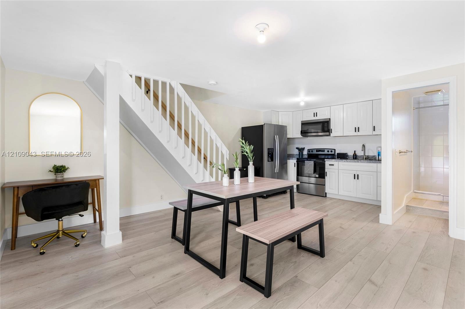 Open-concept kitchen featuring white shaker-style cabinetry, stainless steel appliances, and wood-finish flooring, complemented by a staircase with white balusters