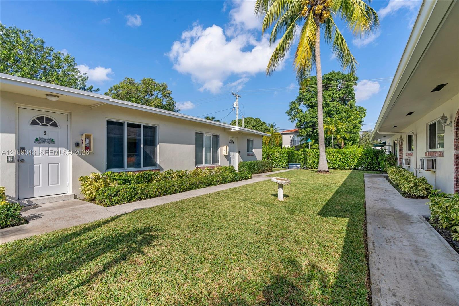 Stucco exterior with multi-panel entry doors, concrete walkways, manicured lawn, and mature palm tree landscaping