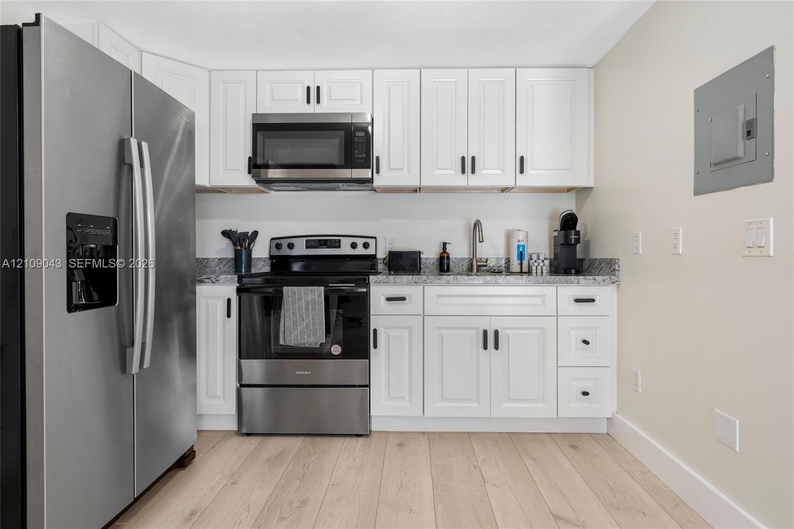 Kitchen featuring white shaker-style cabinetry, stainless steel appliances, speckled stone-finish countertops, and wood-finish flooring