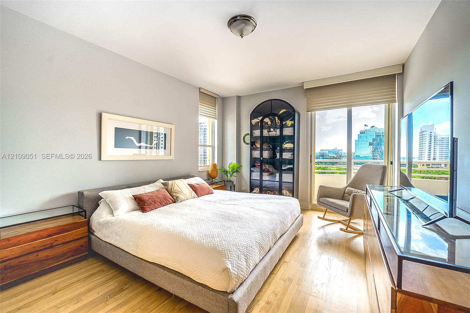 Light-filled room featuring wood-finish flooring, a built-in arched display cabinet with glass shelving, roller shades, and a sliding glass door
