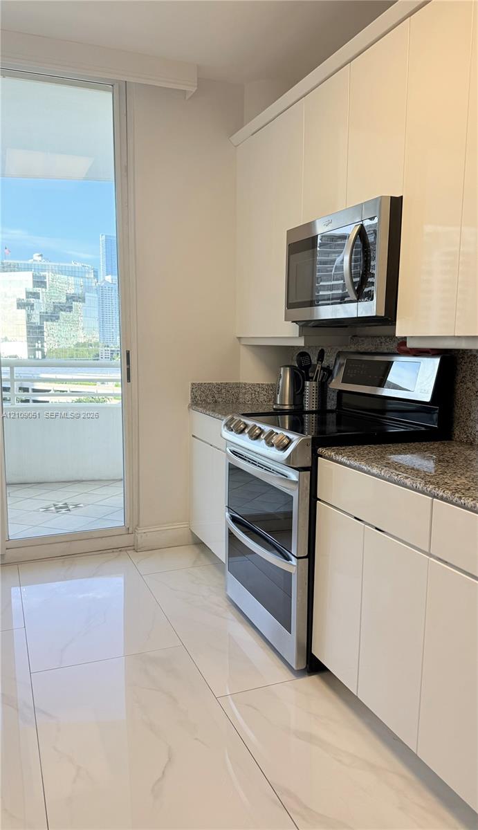 Kitchen featuring high-gloss cabinetry, stone countertops, stainless steel appliances, large-format tile flooring, and access to a balcony