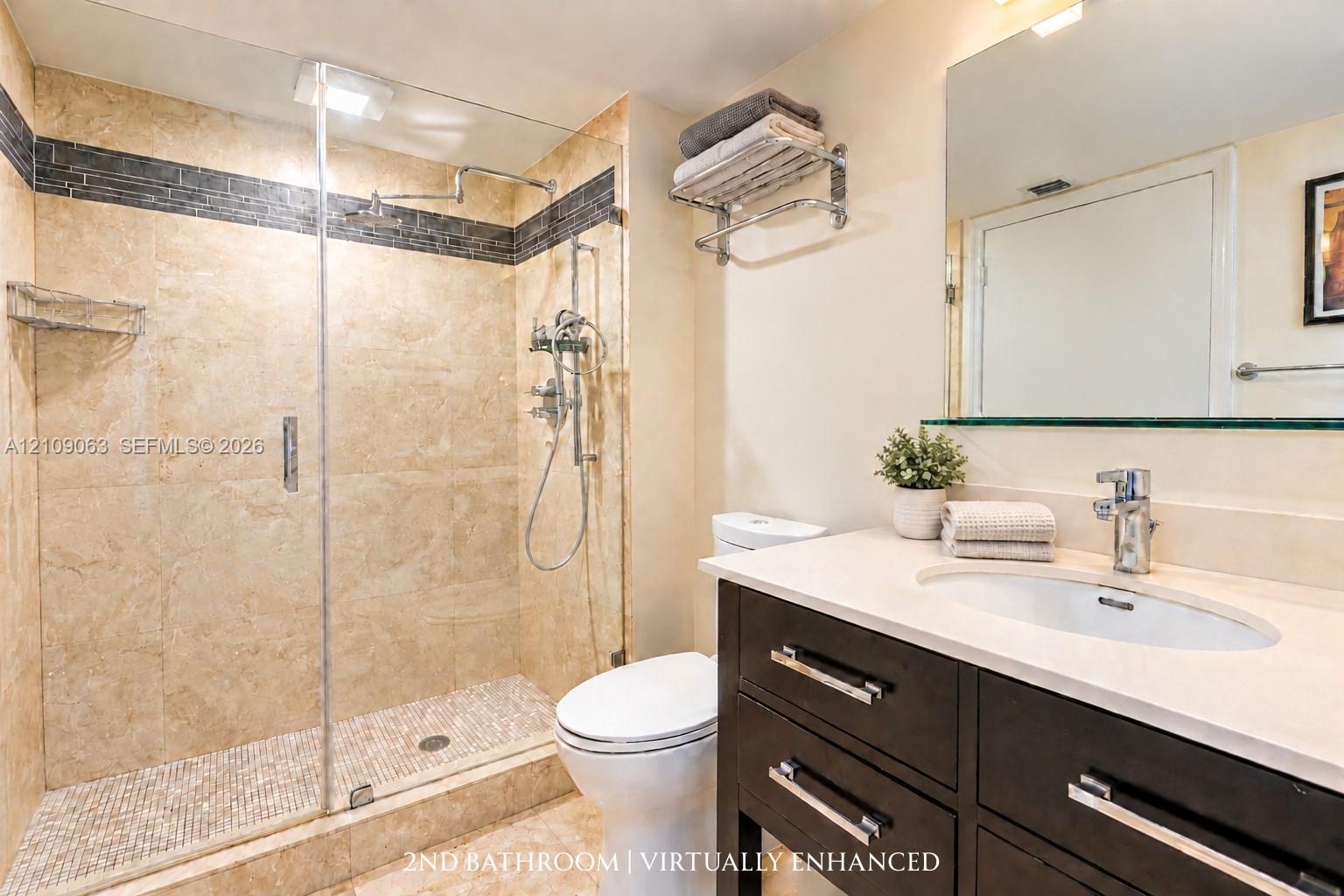Bathroom featuring a walk-in shower with stone tile surround, pebble-style floor, and glass enclosure, complemented by a dark-finish vanity with a light-tone countertop and polished chrome fixtures