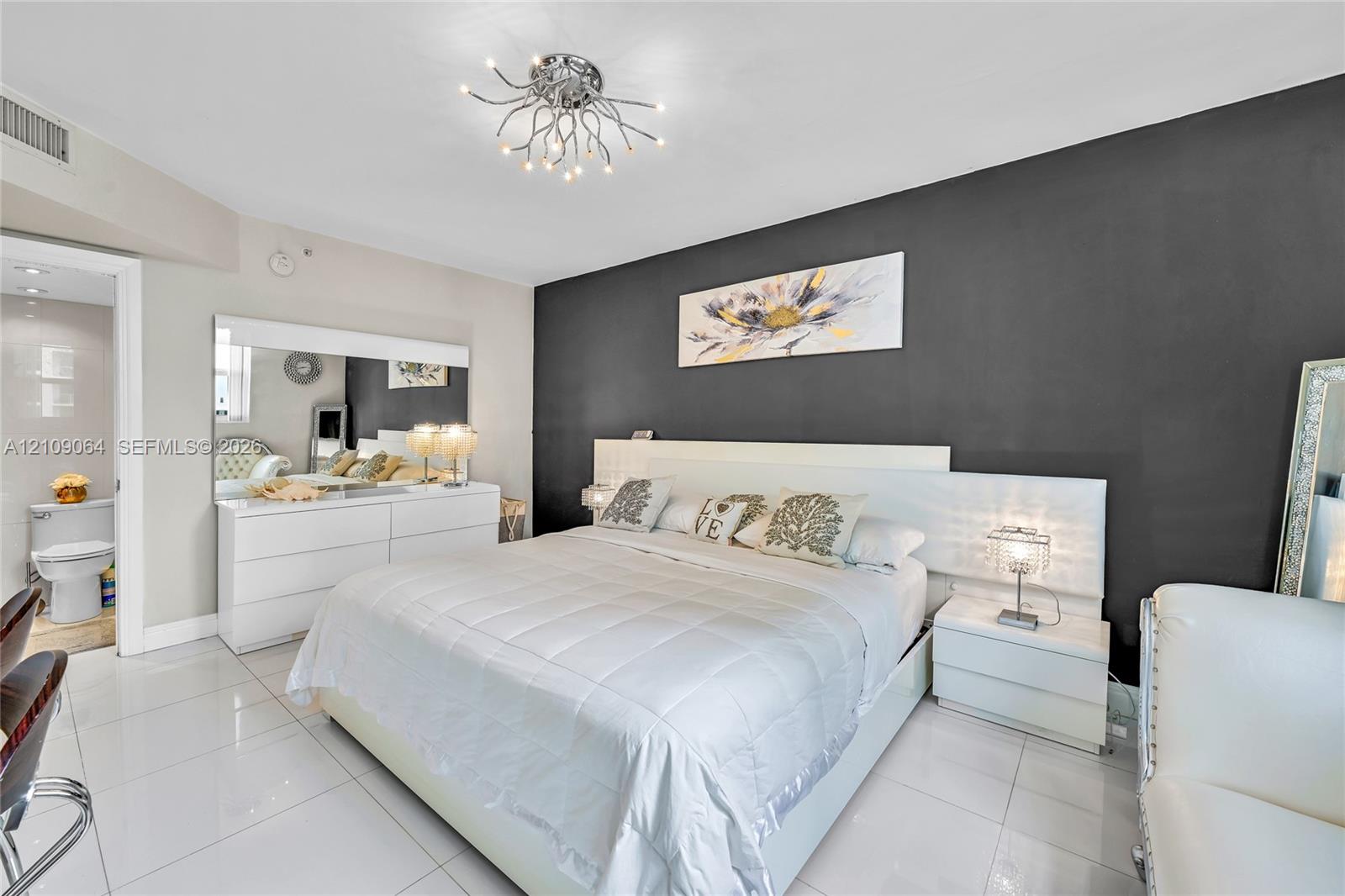 Sleeping area featuring high-gloss white built-in cabinetry, polished tile flooring, a charcoal accent wall, and a contemporary multi-arm chrome chandelier
