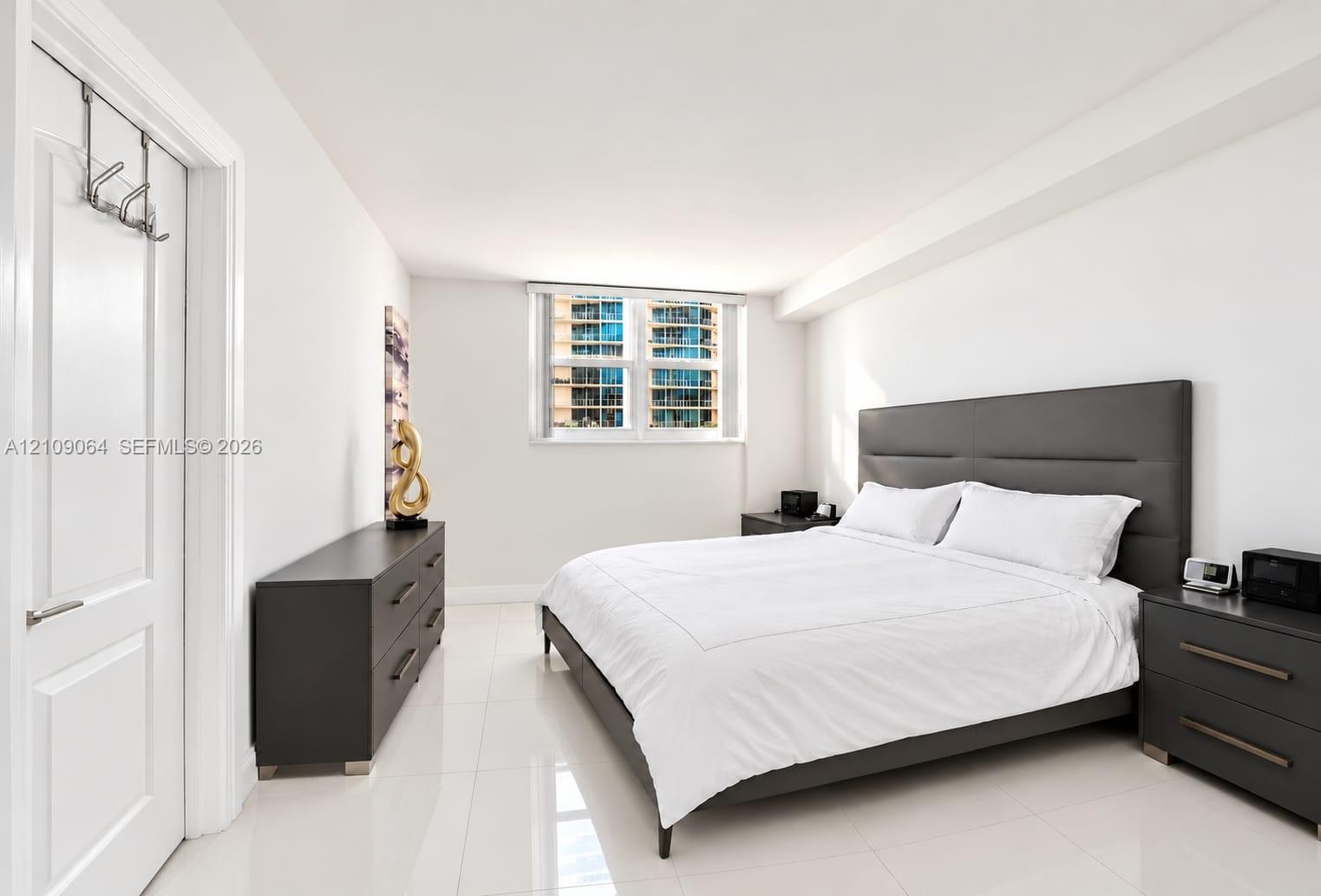 Bright bedroom featuring polished tile flooring, crisp white walls, and a large window