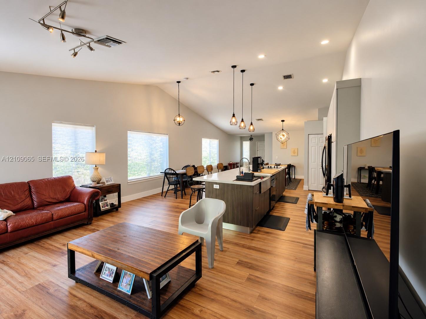 Open-concept space featuring wood-finish flooring, vaulted ceilings, a kitchen island with stone-finish countertops, apron-front sink, and pendant lighting
