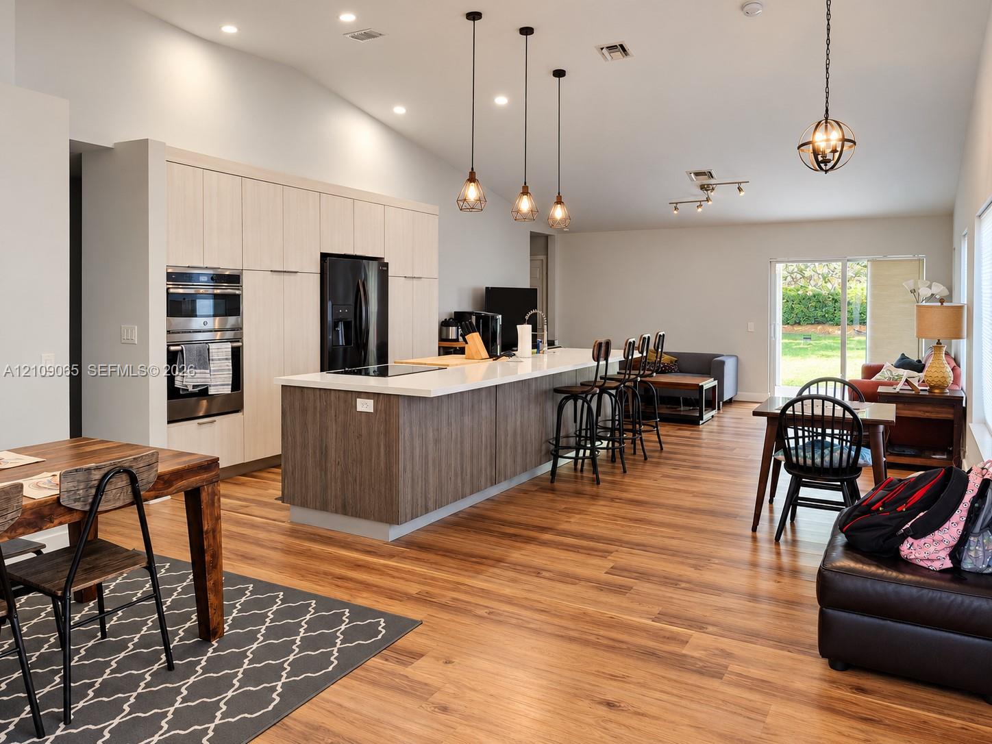 Open-concept kitchen featuring full-height light wood-finish cabinetry, a large center island with contrasting wood-finish paneling and quartz countertops, recessed lighting, and wood-finish flooring throughout