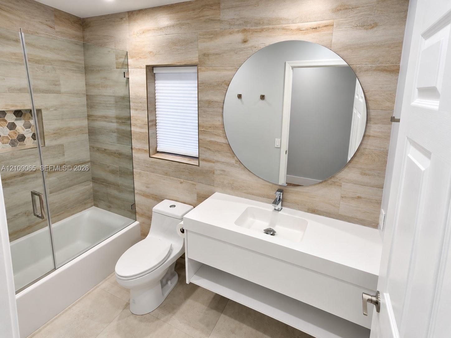 Full-wall wood-finish tile cladding, floating vanity with integrated rectangular basin, frameless glass shower enclosure featuring a built-in recessed niche, and large circular mirror