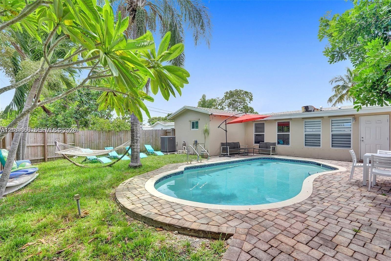 Backyard featuring an in-ground swimming pool, brick paver patio, manicured lawn, and wood-panel perimeter fencing