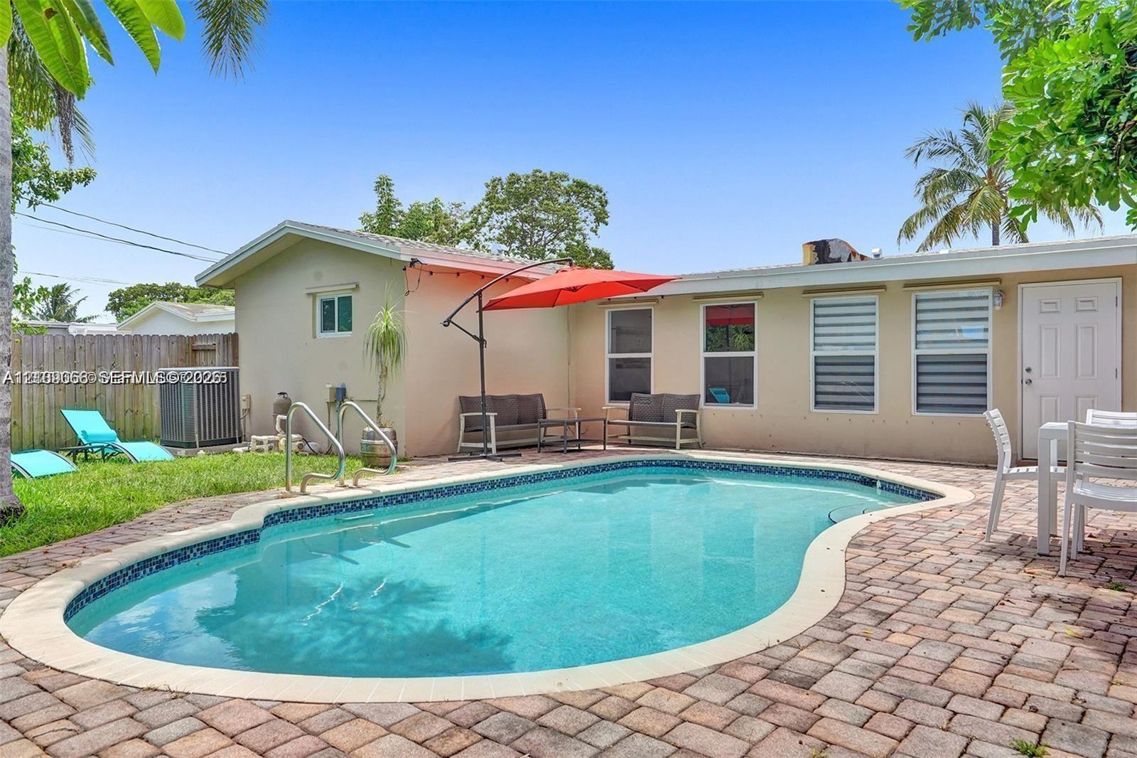 In-ground pool with a curved edge, surrounded by a brick paver patio and a grass lawn enclosed by a wood privacy fence