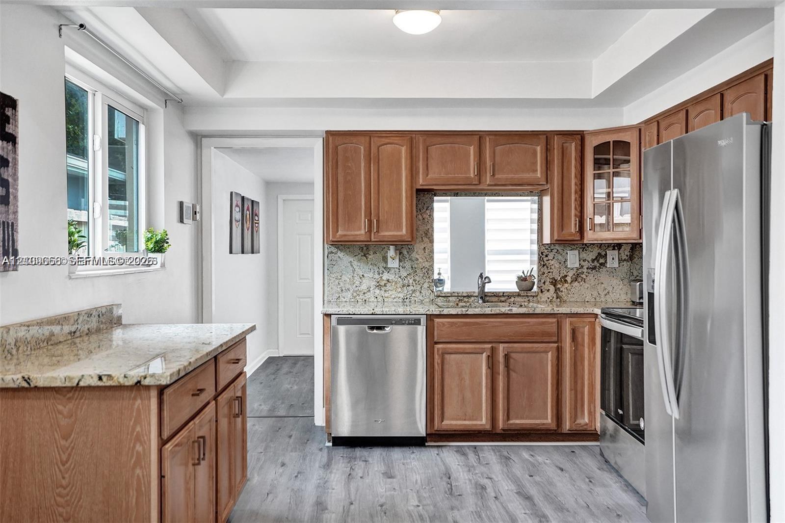 Kitchen featuring wood cabinetry, stone countertops, stainless steel appliances, and wood-finish flooring
