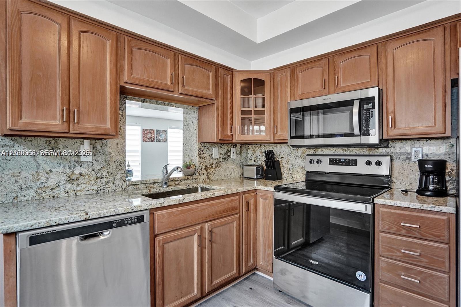 Kitchen featuring wood cabinetry, stone countertops, stainless steel appliances, a glass-panel cabinet door, and a pass-through window