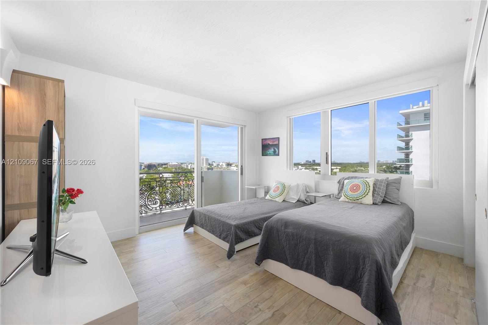 Wood-finish flooring, sliding glass door with balcony access, and large windows with exterior urban scenery Wood-finish flooring, sliding glass door with balcony access, and large windows with exterior urban scenery