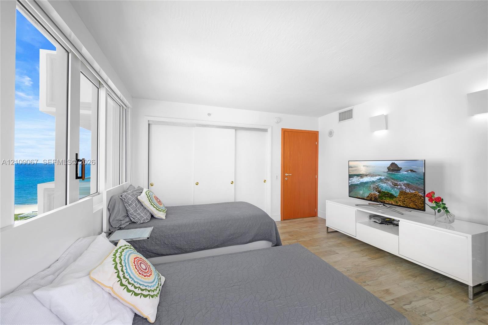 Floor-to-ceiling windows featuring ocean scenery, wood-finish flooring, sliding door closets, and wall-mounted light fixtures